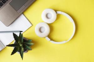 Top view open notepad, headphones pen and laptop on yellow background. workplace photo