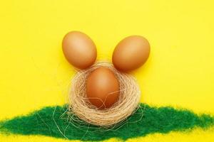 happy easter bunny eggs in nest on the decorative grass on yellow background. copy space for text photo