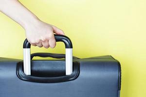 hand holding a suitcase isolated on a yellow background. Air flight journey concept. Copy space mock up photo