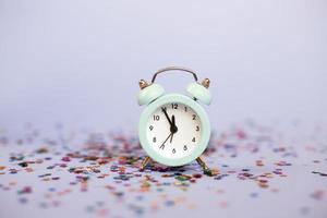 Alarm clock showing five minutes to twelve on a purple background with milticolored sequins photo