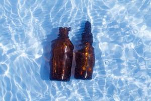 Brown glass oil bottle under fresh water on a blue background. Aromatherapy and perfumes concept photo