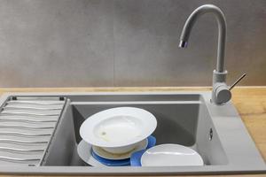 Pile of dirty dishes like plates in the grey modern granite sink in the kitchen photo