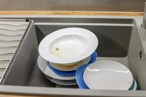 montón de platos sucios como platos en el fregadero de granito gris moderno en la cocina foto