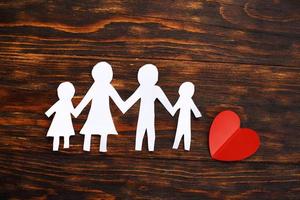 feliz familia cortada en papel tomándose de la mano sobre un fondo de madera marrón con corazón rojo. foto
