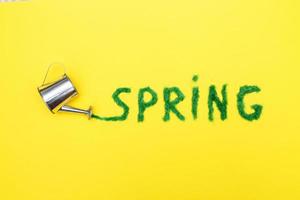 The inscription Spring from decorative green grass on a yellow background with a watering can photo