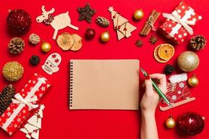 Top view of female hand making some notes in noteebok on colorful background. New Year decorations and toys. Christmas time concept photo