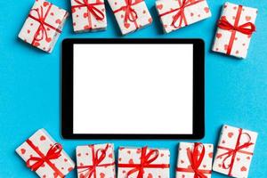 Top view of digital tablet surrounded with gift boxes on colorful background. Saint Valentine's day photo