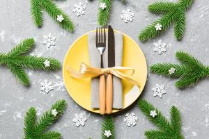 Top view of New Year dinner on festive cement background. Composition of plate, fork, knife, fir tree and decorations. Merry Christmas concept photo