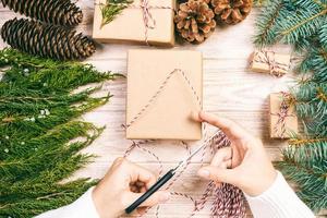 Woman wrapping christmas present , girl prepares xmas gifts with fir tree and pine cone. Hand crafted gift on wooden background with Christmas decor. Top view, copy space. Toned photo