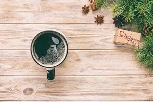 Christmas background with hot coffee, gift box, fir branches and cones on wooden table, top view copy space. Christmas holidays background, flat lay. Toned photo