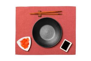 Empty round black plate with chopsticks for sushi and soy sauce, ginger on red napkin background. Top view with copy space for you design photo