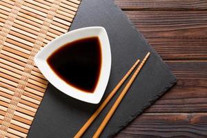 Chopsticks and soy sauce on black stone plate, wooden background with copy space photo