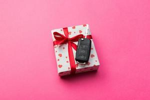 Car key on paper gift box with red ribbon bow and heart on pink table background. Holidays present top view concept photo