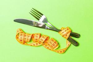 Diet concept with fork, knife and measuring tape on green background. Top view of weight loss photo