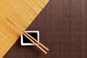 Chopsticks and bowl with soy sauce on two bamboo mat blak and yellow top view with copy space photo