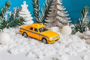 Christmas banner Background. Yellow toy car Taxi Cab model and winter decorations ornaments on blue background with snow. City traffic delivery taxi service concept. photo