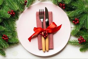 Holiday composition of plate and flatware decorated with fir tree on wooden background. Top view of Christmas decorations. Festive time concept photo
