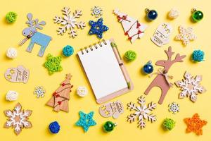 Top view of notebook on yellow background with New Year toys and decorations. Christmas time concept photo