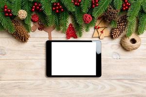 Top view of tablet, Christmas toys, decorations and fir tree branches on wooden background. New Year holiday concept with copy space photo