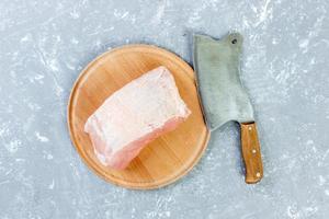 Raw cut of pork shoulder on board with knife or Kitchen ax. cleaver with fresh raw meat on gray concrete background photo