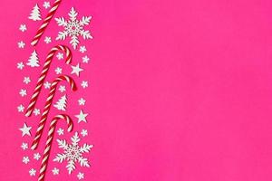 Christmas candy cane lied evenly in row on pink background with decorative snowflake and star. Flat lay and top view photo