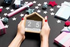 Top view of female hands holding calendar on black background. The twenty fifth of December. Holiday decorations. Christmas time concept photo