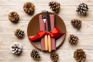 New Year set of plate and utensil on wooden background. Top view of holiday dinner decorated with pine cones. Christmas time concept