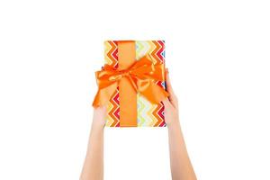 Woman hands give wrapped Christmas or other holiday handmade present in colored paper with orange ribbon. Isolated on white background, top view. thanksgiving Gift box concept photo