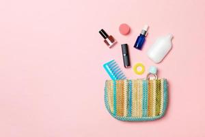 Make up products spilling out of cosmetics bag on pink pastel background with empty space for your design photo