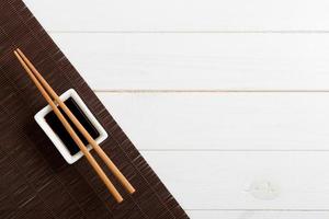 Bamboo mat and soy sauce with sushi chopsticks on white wooden table. Top view with copy space background for sushi. Flat lay photo