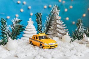 fondo de la bandera de navidad. modelo de taxi de coche de juguete amarillo y adornos de invierno sobre fondo azul con nieve. concepto de servicio de taxi de entrega de tráfico de la ciudad. foto