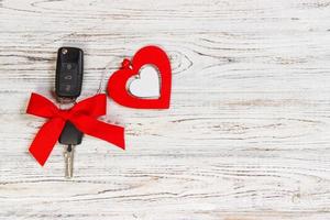 Car key with a red ribbon adn a heart on white wooden table. Giving present or gift for valentine's day or christmas photo