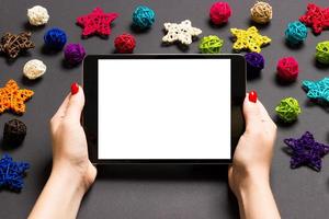 Top view of woman holding tablet in her hands on black background made of Christmas decorations. New Year holiday concept. Mockup photo