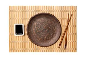 Empty round brown plate with chopsticks for sushi and soy sauce on yellow bamboo mat background. Top view with copy space for you design photo