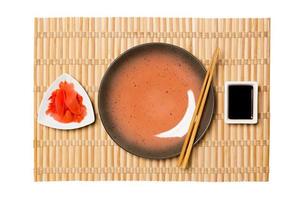 Empty round brown plate with chopsticks for sushi and soy sauce, ginger on yellow bamboo mat background. Top view with copy space for you design photo