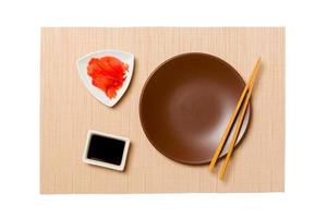 Empty round brown plate with chopsticks for sushi and soy sauce, ginger on brown sushi mat background. Top view with copy space for you design photo