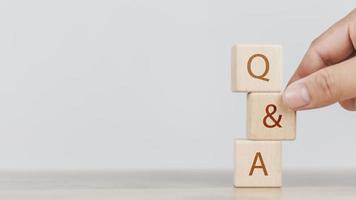 una mano de hombre sosteniendo q y una palabra con bloque de cubo de madera. preguntas frecuentes, servicio al cliente comercial y soporte foto