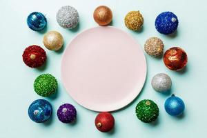 Top view of empty plate surrounded with colorful baubles on blue background. New Year decorations. Christmas Eve concept photo