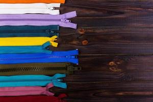 Multicolored zippers are laid out on a wooden table photo