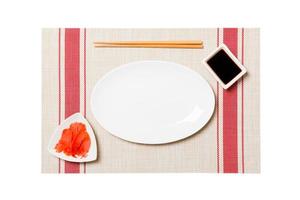 Empty oval white plate with chopsticks for sushi and soy sauce, ginger on sushi mat background. Top view with copy space for you design photo