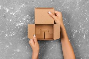 manos de mujer sosteniendo una caja vacía sobre fondo gris, vista superior en el estudio foto