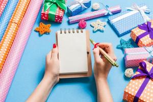 Top view of female hand making some notes in noteebok on blue background. New Year decorations and toys. Christmas time concept photo