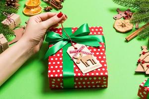 Top view of female hands holding a Christmas present on festive green background. Fir tree and holiday decorations. New Year holiday concept photo