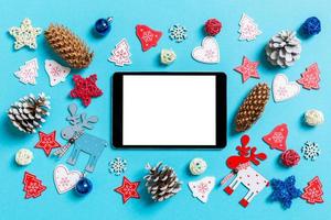 Top view of digital tablet surrounded with New Year toys and decorations on blue background. Christmas time concept photo