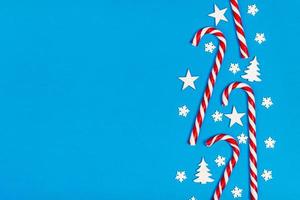 Christmas candy cane lied evenly in row on blue background with decorative snowflake and star. Flat lay and top view photo