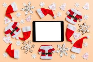 Top view of digital tablet with Christmas decorations and Santa hats on orange background. Happy holiday concept photo