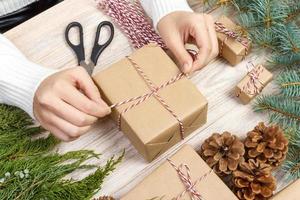 Christmas presents preparation. Gift box wrapped in black and white striped paper, a crate full of pine cones and christmas toys and wrapping materials on a white wood old background photo