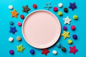 Top view of holiday plate decorated with knitted baubles and stars on colorful background. New Year decorations and toys. Family Christmas dinner concept photo
