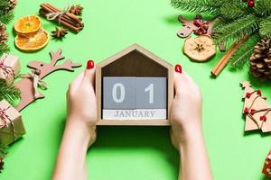 Top view of female hands holding calendar on green background. The first of January. Holiday decorations. New Year concept photo