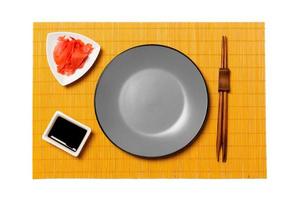 Empty round gray plate with chopsticks for sushi and soy sauce, ginger on yellow bamboo mat background. Top view with copy space for you design photo